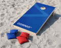 Cornio essential bags in the beach with a cornio cornholegame in the back